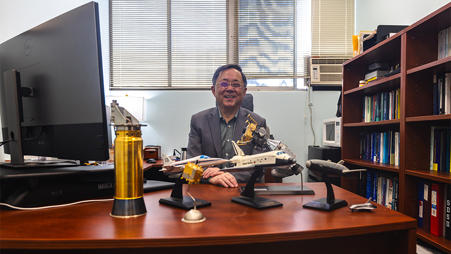 Ping Lu smiling in his office surrounded by models of spacecraft and aircraft.